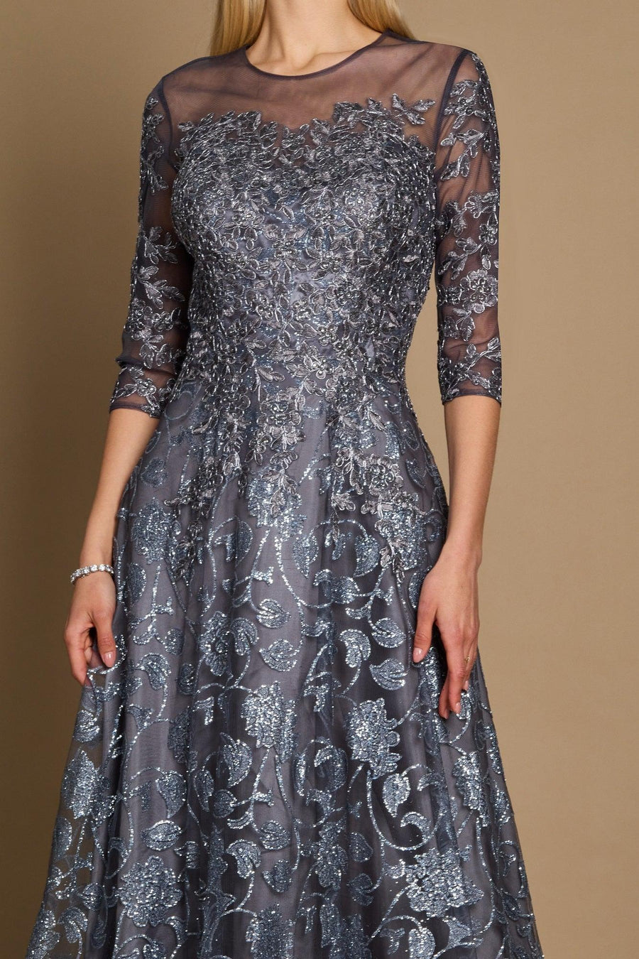 A long formal evening dress in charcoal gray, featuring intricate lace detailing and a flowing silhouette, elegantly draping to the floor.